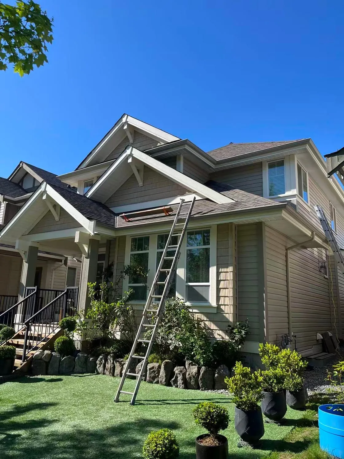 Sage-green craftsman house with cream trim under a clear sky, a ladder against the gutter