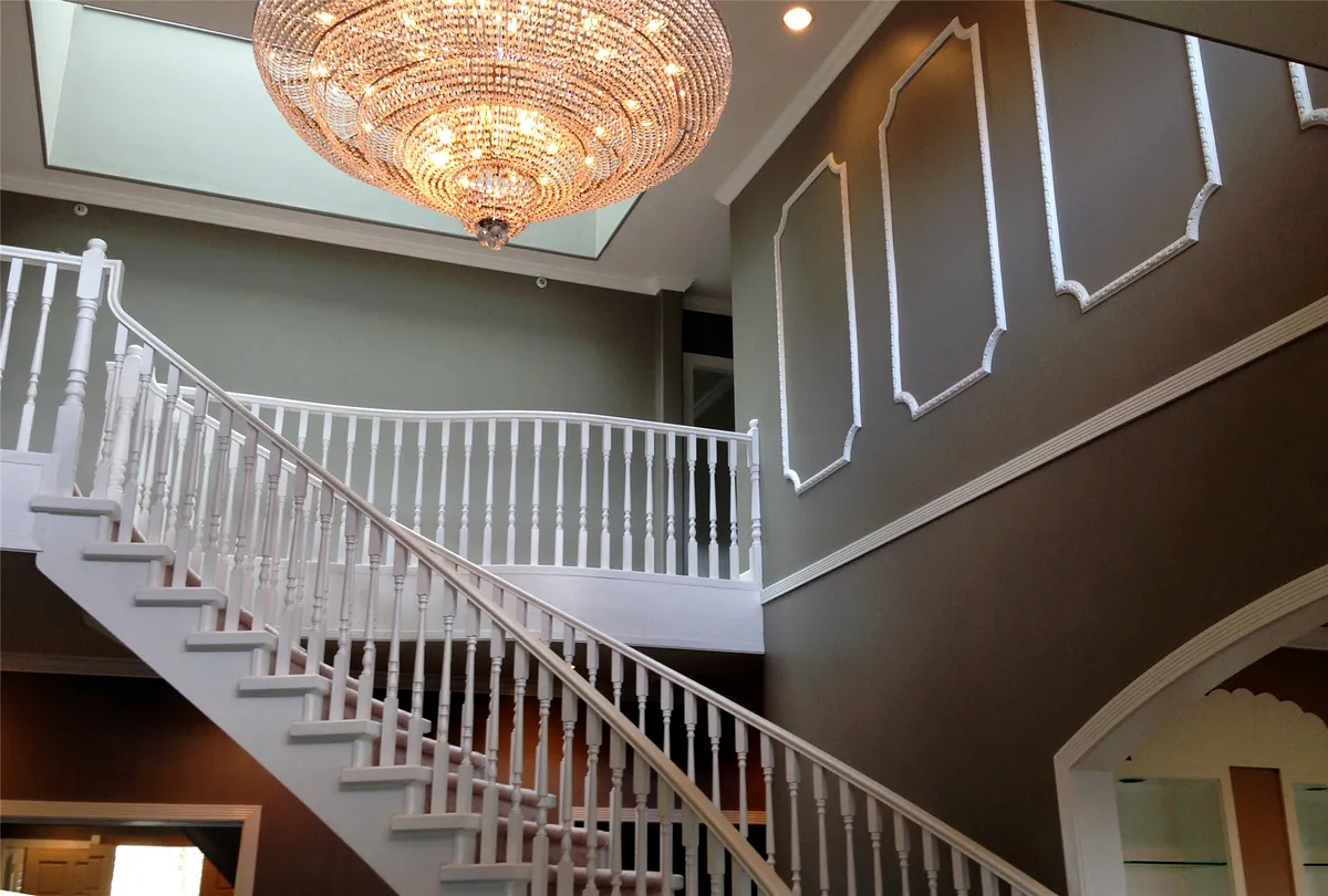 Staircase with grey-green walls, white panelling and a chandelier in natural light